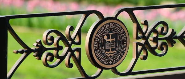 Close up of a wrought iron gate featuring the Notre Dame seal and pink tulips in the background.