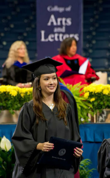 A female graduate wearing a cap and gown holding her diploma at the A&L Diploma Ceremony.