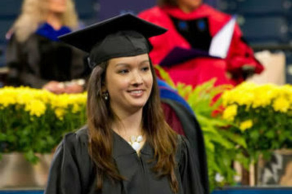 A female graduate wearing a cap and gown holding her diploma at the A&L Diploma Ceremony.