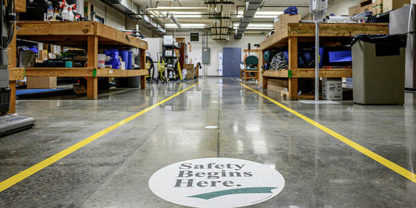 A campus workshop with a decal on the floor that reads "Safey Begins Here."