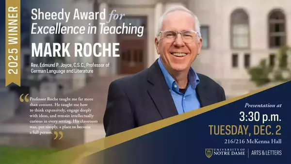 Mark Roche, smiling broadly, wears glasses, a blue shirt, and a dark jacket against a blurred Notre Dame campus building with stone walls and arched windows.